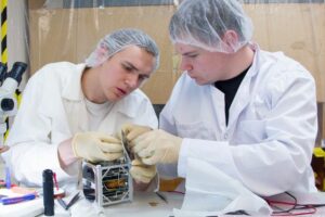  Vasakult TÜ arvutitehnika üliõpilane Erik Ilbis (Tallinna Reaalkoolist), füüsikadoktorant Mihkel Pajusalu (õppinud Treffneris ja Tartu Tamme Gümnaasiumis) monteerivad satelliiti kokku.