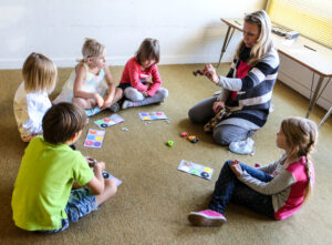 Keeleõpetaja Leelo Kask kutsub lapsed põrandale ringi ja värvikaartide abil uuritakse üheskoos tuttavaid numbreid ja sõnu. 